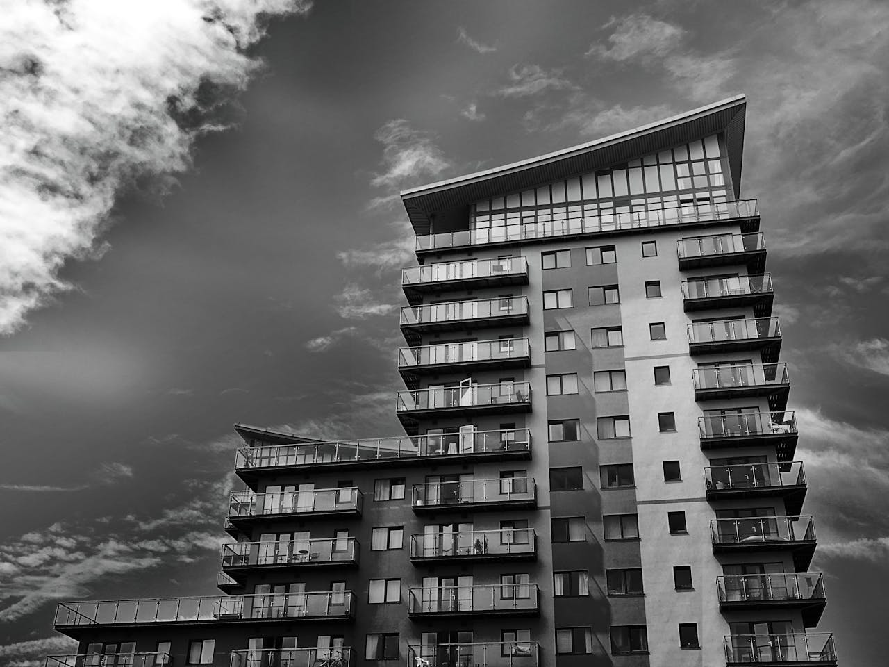 Monochrome photo of a modern high-rise apartment building with dynamic sky.